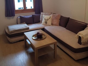 Ein modernes Wohnzimmer mit einer Eckcouch, einem kleinen Holztisch und einem Fenster mit Vorhängen.