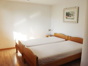 Ein Zimmer mit zwei Holzbetten, einem Nachttisch mit Lampe und einem gerahmten Bild an der Wand.