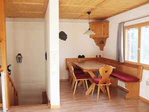 Ein Essbereich aus Holz mit Tisch und Bänken, einem an der Wand befestigten Regal und einem Fenster mit Vorhängen.