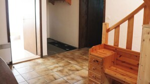Um quarto com escada de madeira, piso de azulejos e porta que dá para outro cômodo.