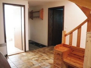 Ein Zimmer mit einer Holztreppe, gefliestem Boden und einer Tür zu einem weiteren Raum.