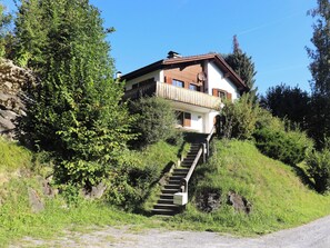 Ein zweistöckiges Haus mit Balkon, umgeben von Grünflächen und einer Steinmauer.