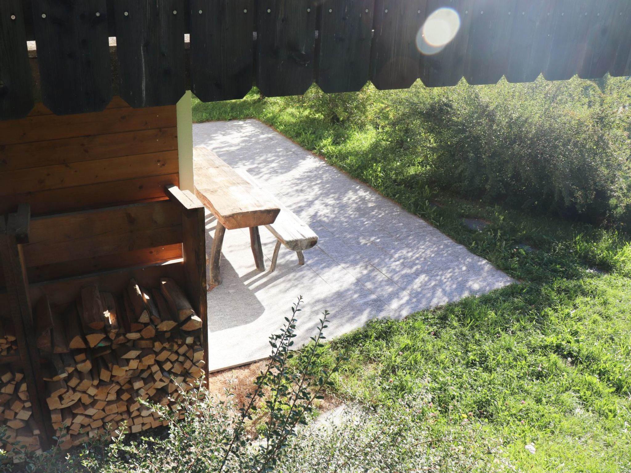 A wooden bench and picnic table in a backyard with a fire pit and firewood.