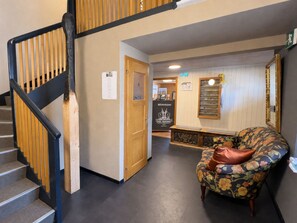 A hotel lobby with a staircase, a wooden door, a bench, and a floral armchair.