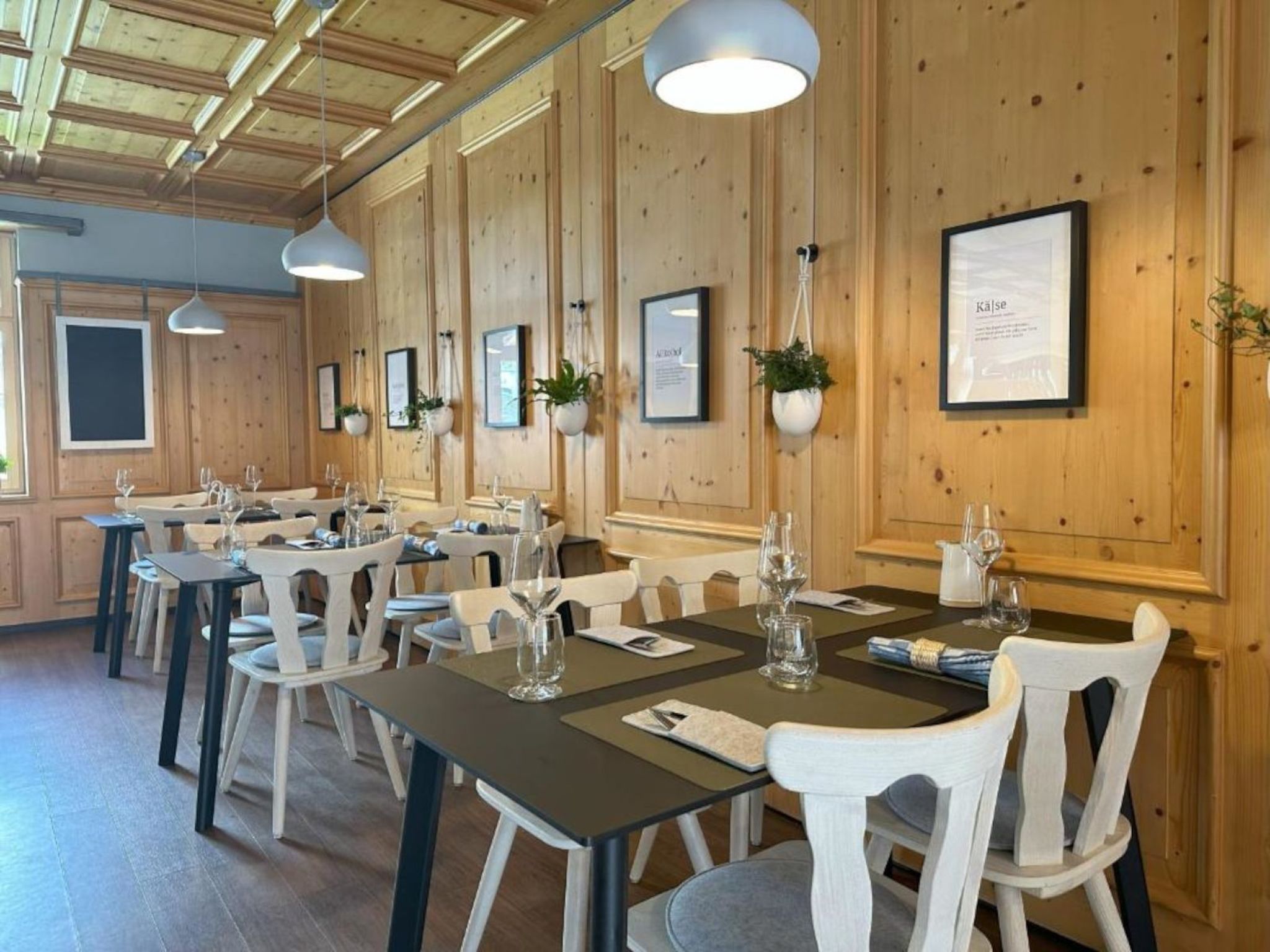 A dining area with wooden walls, multiple tables, and chairs, some with plants.