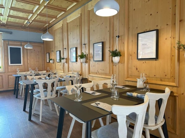 A dining area with wooden walls, multiple tables, and chairs, some with plants.