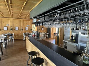 A bar area with a long counter, multiple stools, and a ceiling with wooden beams.