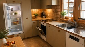 Kompakti keittiö, jossa on sisäänrakennettu jääkaappi, liesi, uuni ja pesuallas. Keittiössä on puinen pöytä, jonka päällä on hedelmäkulho ja kynttilä.