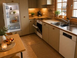 A compact kitchen with a built-in refrigerator, a stove, oven, and a sink. There is a wooden table with a bowl of fruit and a candle.