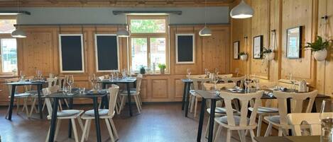 Un restaurante con paredes y techo de madera, varias mesas con sillas y lámparas colgantes.