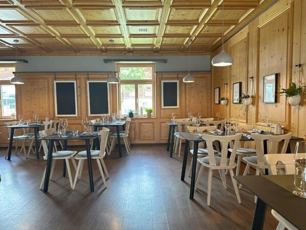 A restaurant with wooden walls and ceiling, multiple tables with chairs, and hanging pendant lights.
