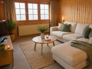 A cozy living room with a sofa, a coffee table with a vase and candle, and a television on a wooden table.