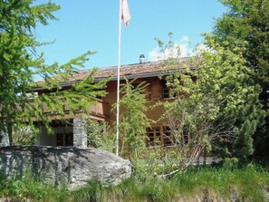 A wooden cabin with a stone foundation, surrounded by trees and a large rock.