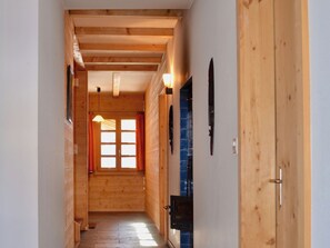 A wooden interior hallway with a door on the right, a window with curtains, and a hanging light fixture.