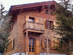 A wooden chalet with a balcony, large windows, and a stone foundation.