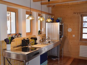 A modern kitchen with stainless steel appliances, a central island, pendant lighting, and wooden paneling.