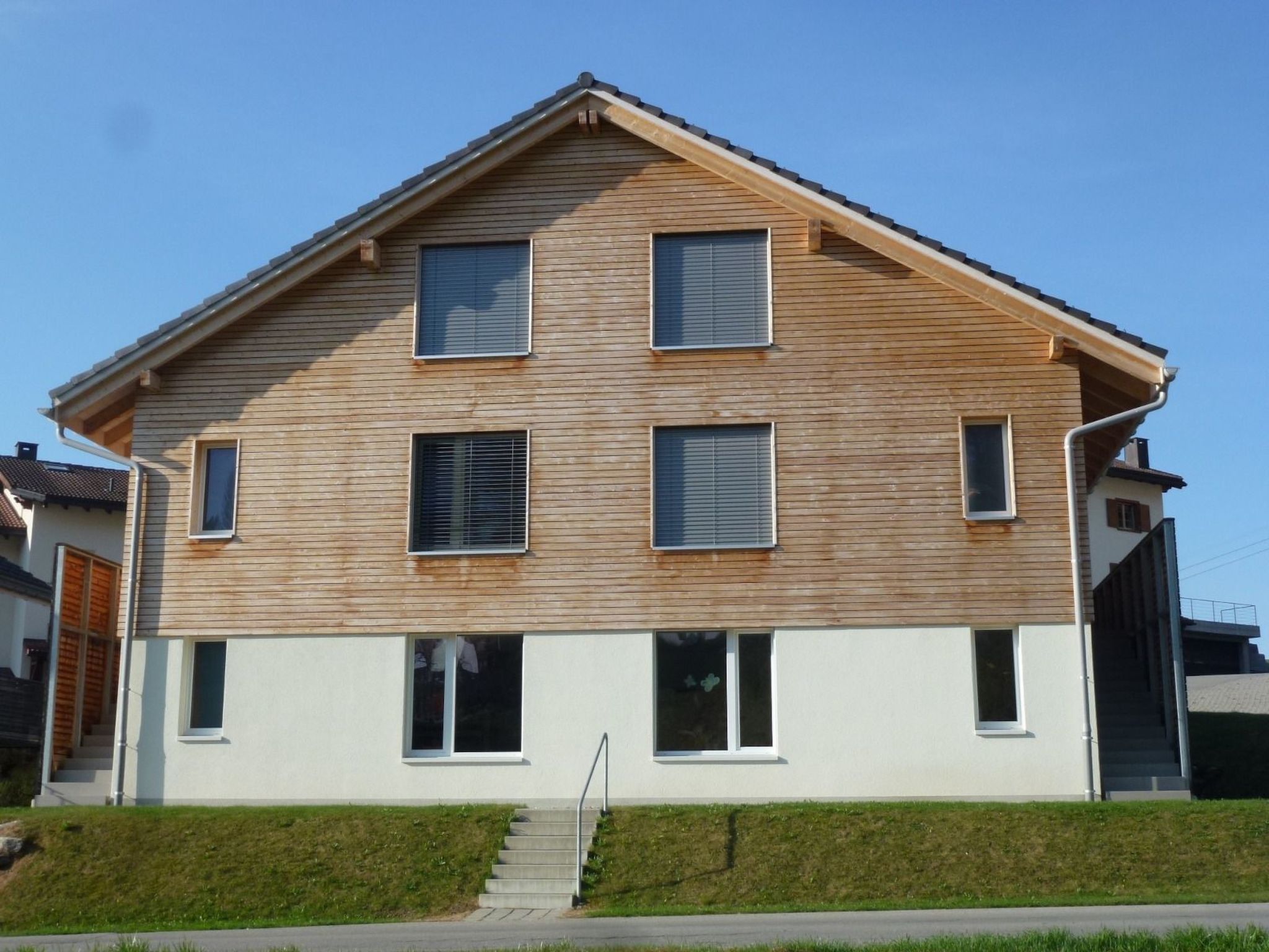 Un bâtiment à deux étages, doté d’un toit en pente, de nombreuses fenêtres et d’un escalier apparent menant à l’entrée.