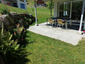 A patio area with a table and chairs, surrounded by a grassy lawn and a stone wall.