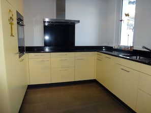 A kitchen with a black range hood, beige cabinets, and a window with a view.