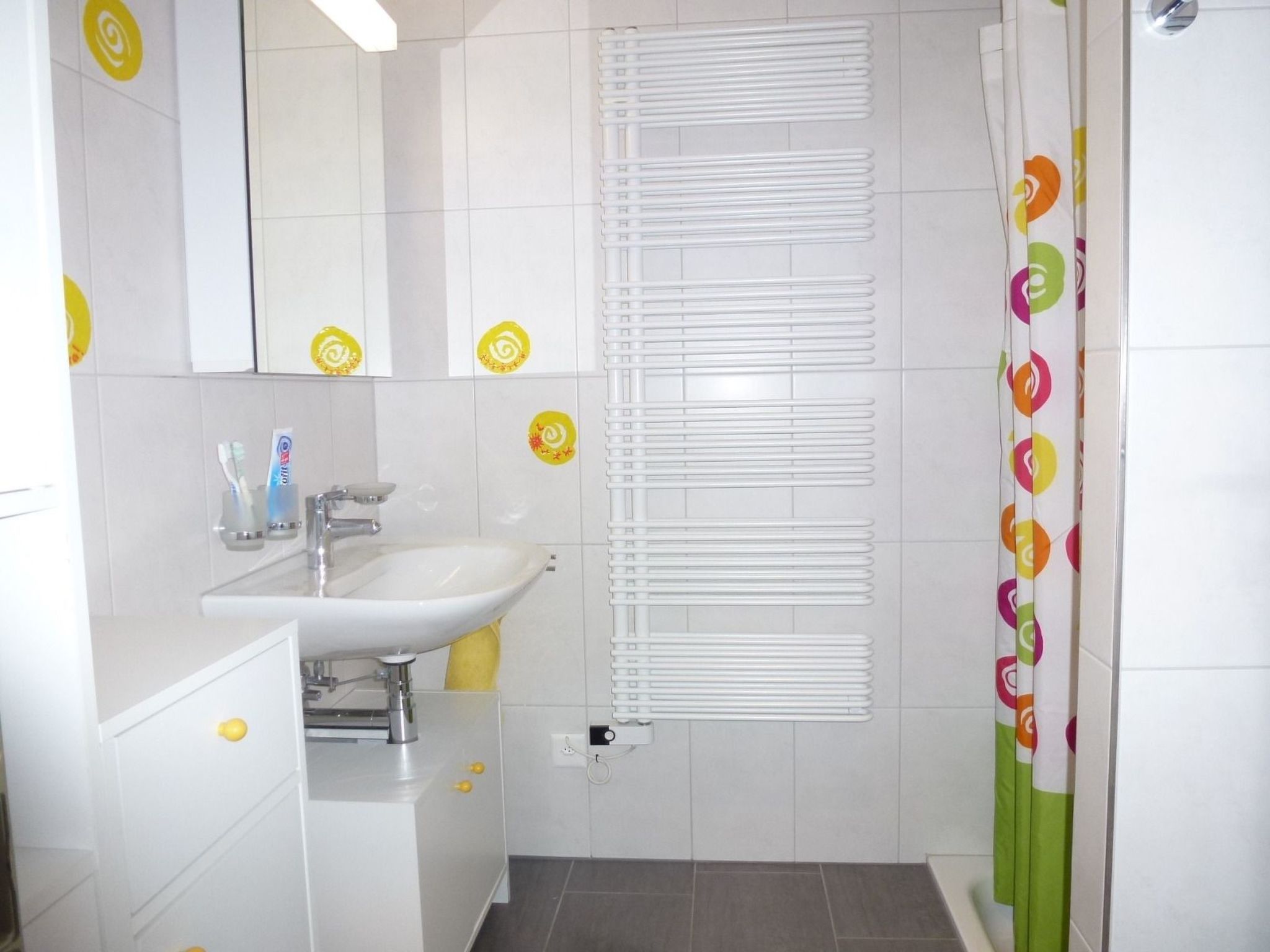 Een badkamer met een wit wastafel, spiegel en een douchegordijn met een kleurrijk patroon.
