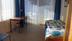 A room with a bed, a desk, and a chair. There is a window with curtains, and a view of the outside. - Denter Uauls Jucker, Vella, (Vella), 44012B by Interhome (Vella)