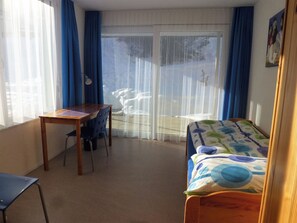 A room with a bed, a desk, and a chair. There is a window with curtains, and a view of the outside. - Denter Uauls Jucker, Vella, (Vella), 44012B by Interhome (Vella)