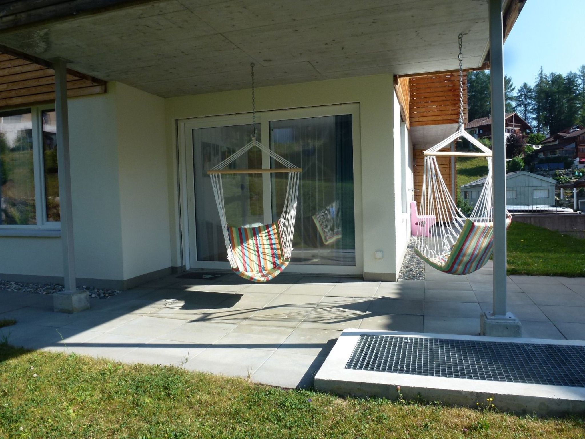 Een modern gebouw met een overdekte veranda, twee hangstoelen en een glazen entree.