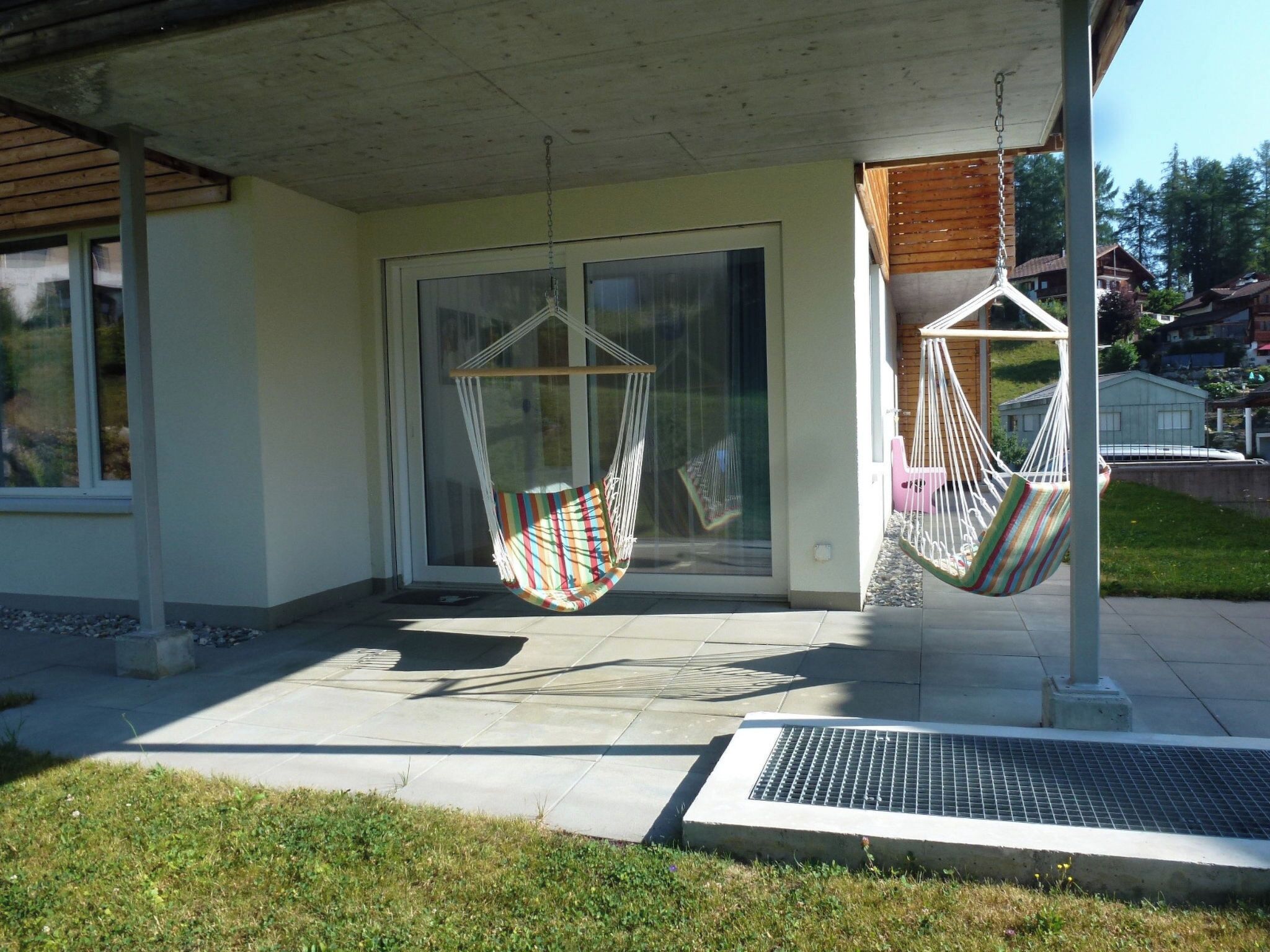 A modern building with a covered porch, two hammock chairs, and a metal grate.