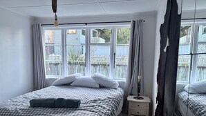 A bedroom with a bed, bedside tables, a lamp, and a window with curtains. - Lorenzen Bay Bungalow by The Sea (Raglan)