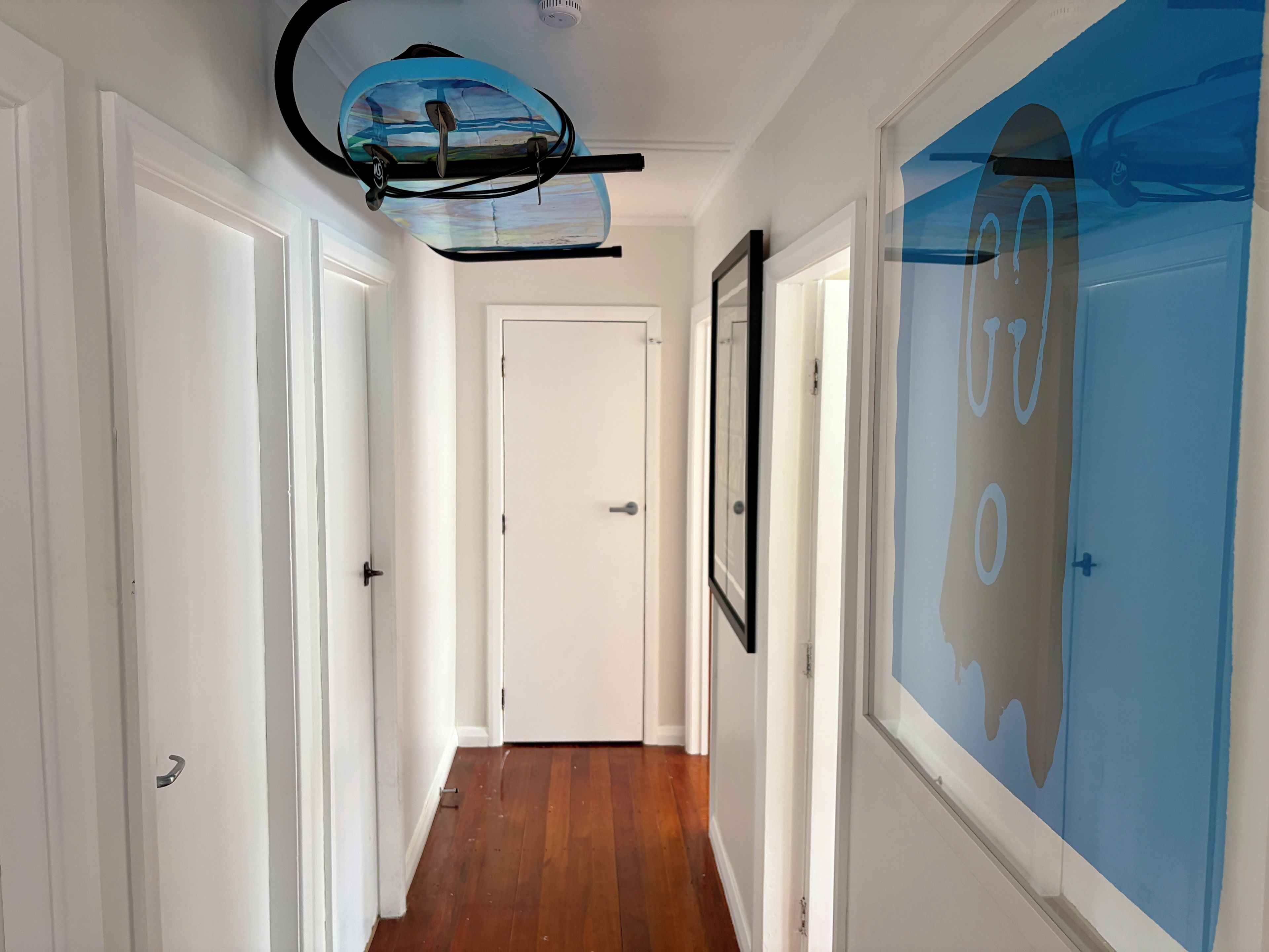 A hallway with wooden flooring, white doors, and a ceiling fan.