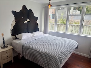 Un dormitorio con cama, mesita de noche, cabecero fijado a la pared y ventana con vistas al exterior.