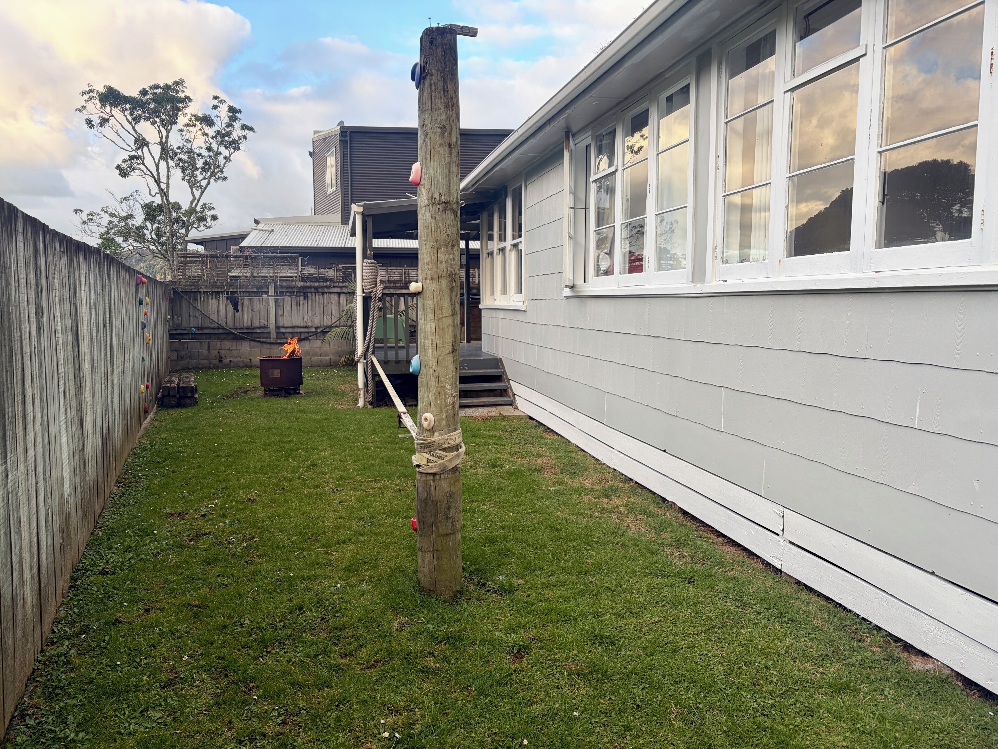 Un jardin avec une clôture en bois, une pelouse verdoyante, un poteau électrique en bois et un bâtiment aux murs et fenêtres blancs.