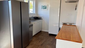 A kitchen with a stainless steel refrigerator, a wooden countertop, white cabinets, and a window providing natural light. - Lorenzen Bay Bungalow by The Sea (Raglan)