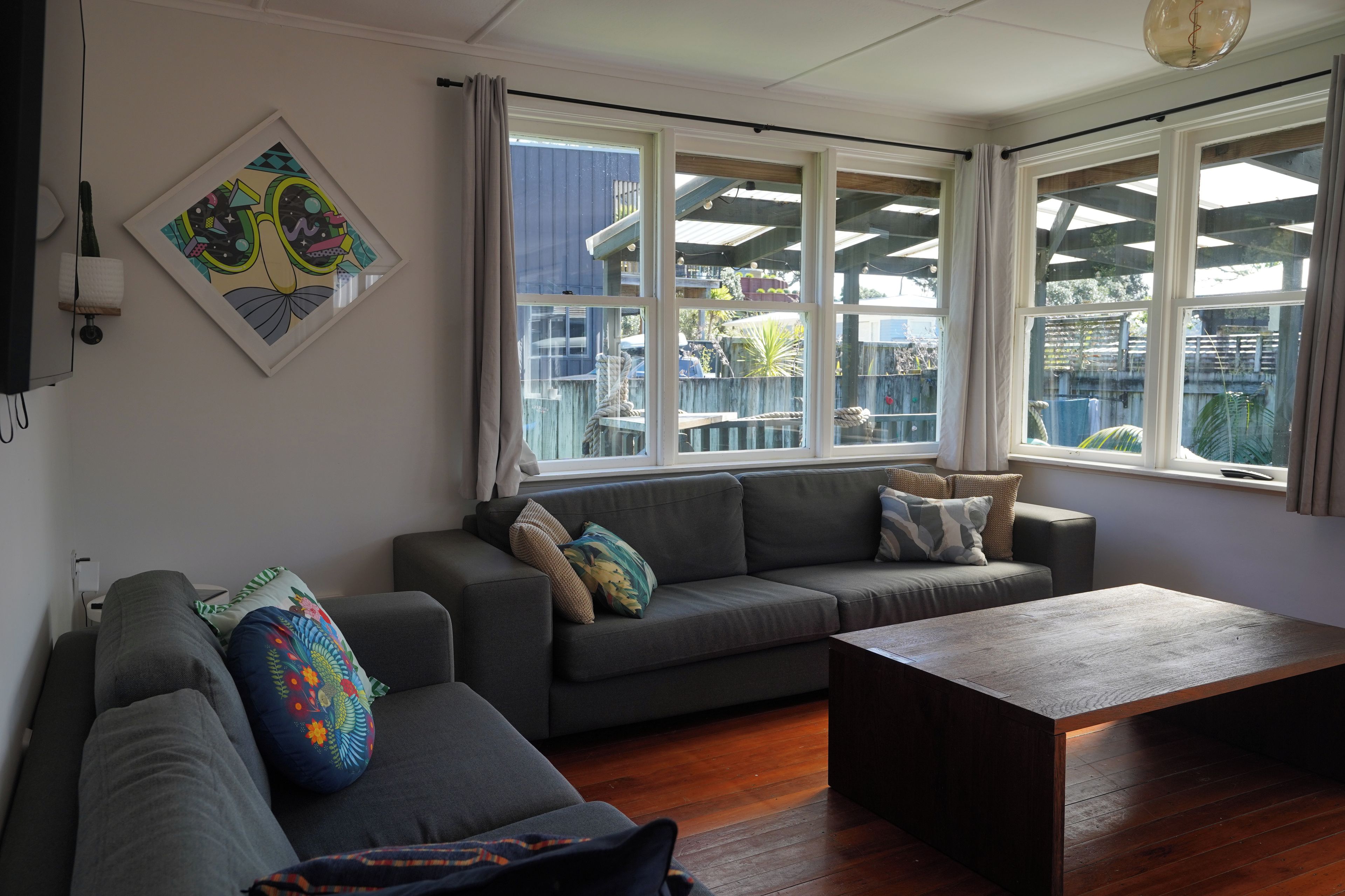 A living room with a grey sofa, a wooden coffee table, and a large window with curtains.
