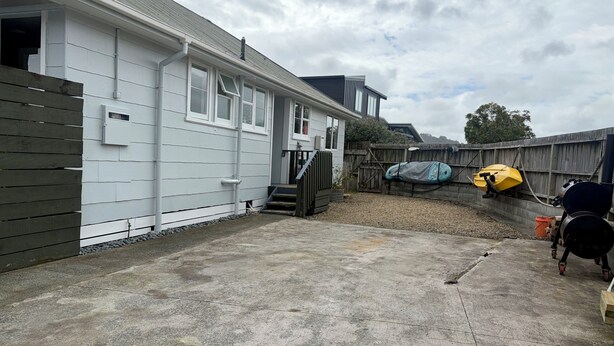 A residential backyard with a concrete patio, a wooden fence, and a yellow kayak. - Lorenzen Bay Bungalow by The Sea (Raglan)
