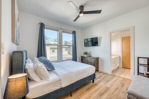 Quarto com cama, ventoinha no teto, televisão e janela.