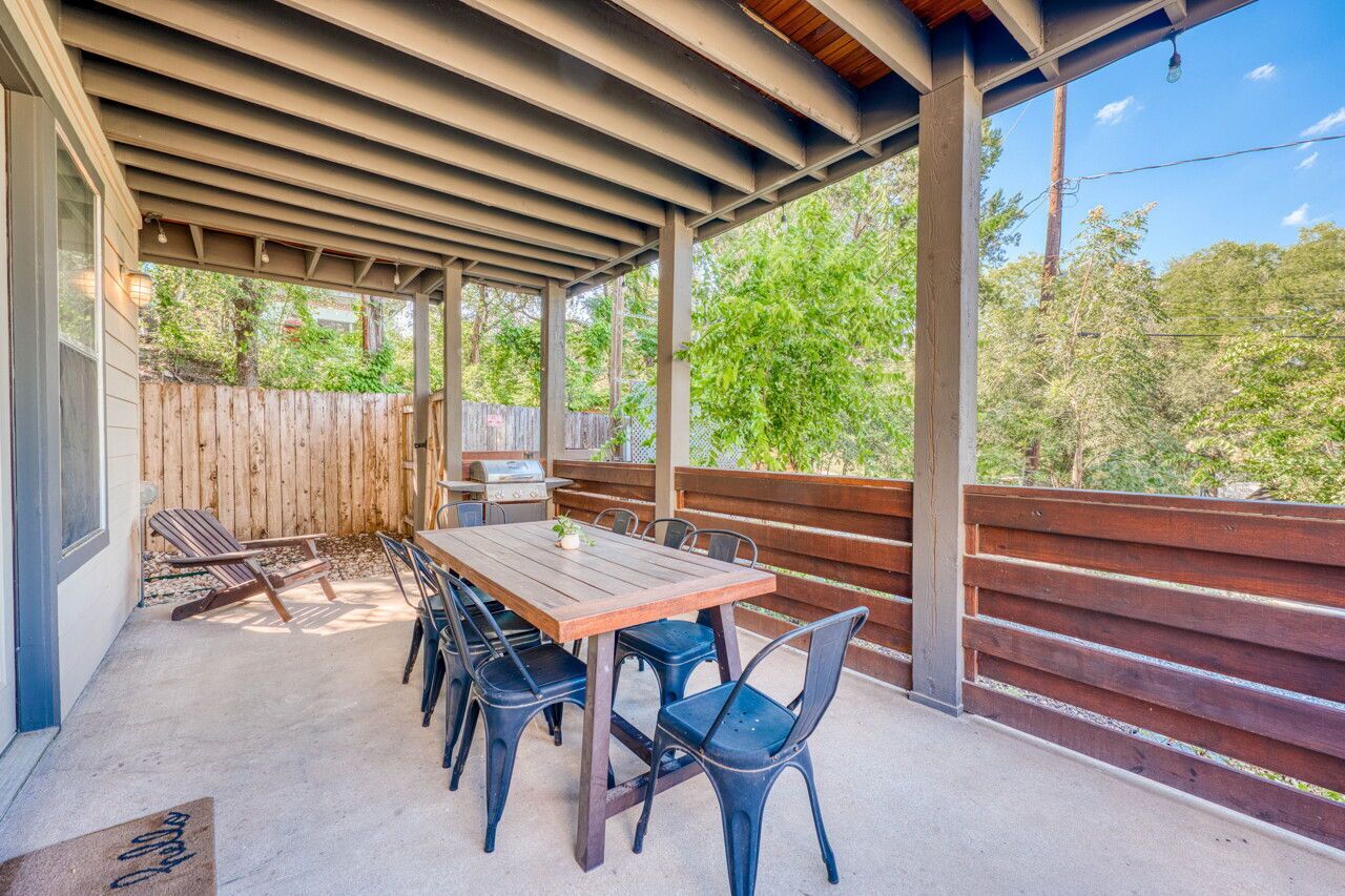Eine Terrasse im Freien mit Holztisch und -stühlen, einem Grill und einem Holzzaun.