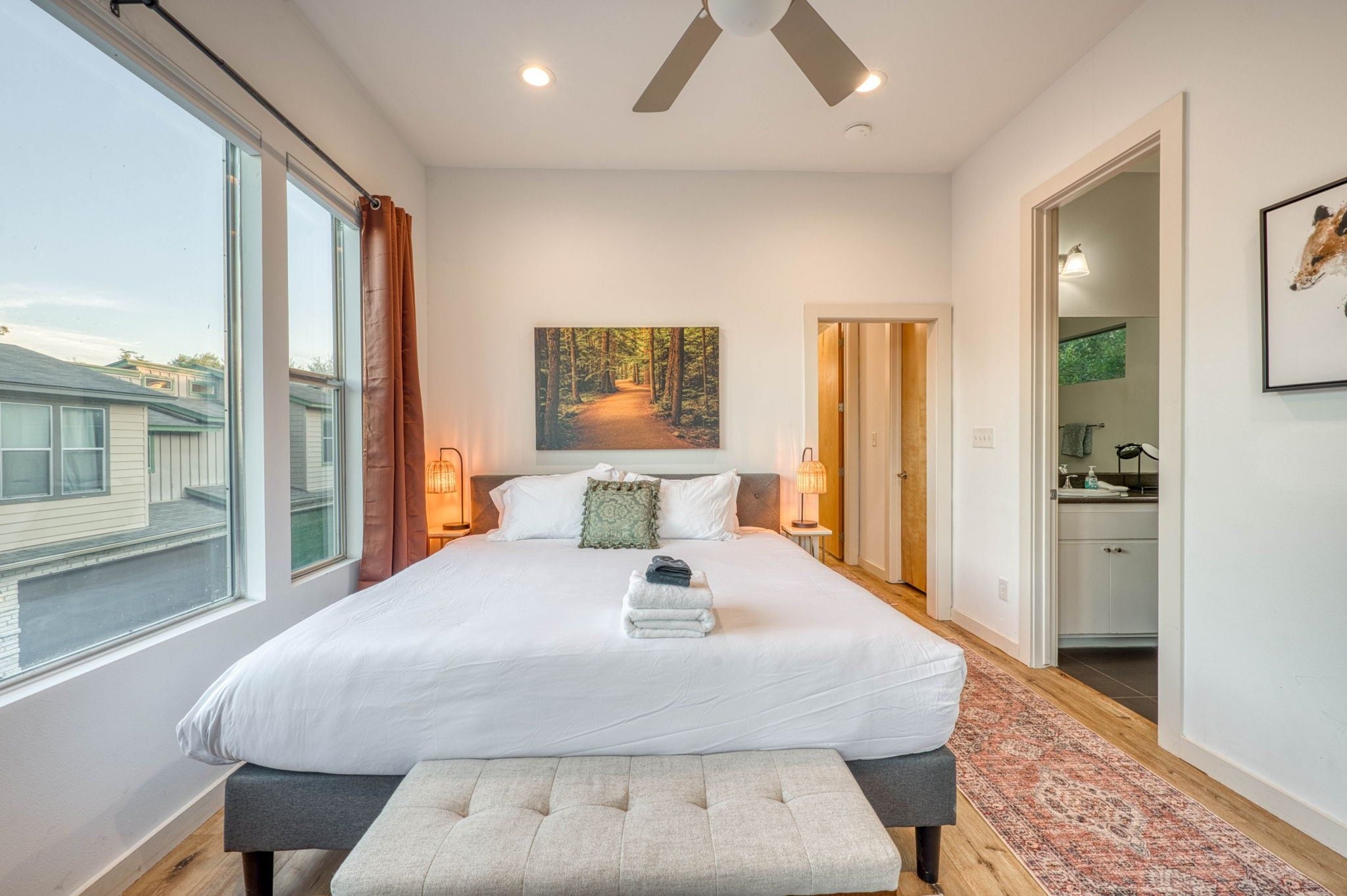 Een slaapkamer met een groot bed, nachtlampjes, een schilderij en uitzicht op het omliggende landschap.