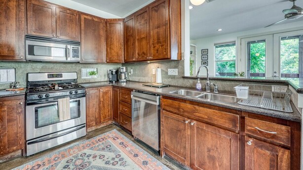 A kitchen with wooden cabinets, stainless steel appliances, and a large window providing natural light. - *New* Austin Skyline Vista 🦚 | Rooftop Views, South First Vibes 🌵🎸 (Austin)