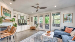A spacious living area with a ceiling fan, a sofa, a coffee table, and a kitchen area with a TV. - *New* Austin Skyline Vista 🦚 | Rooftop Views, South First Vibes 🌵🎸 (Austin)