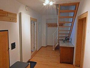 A hallway with a wooden staircase leading to a loft area, a door with a handle, and a small bench.
