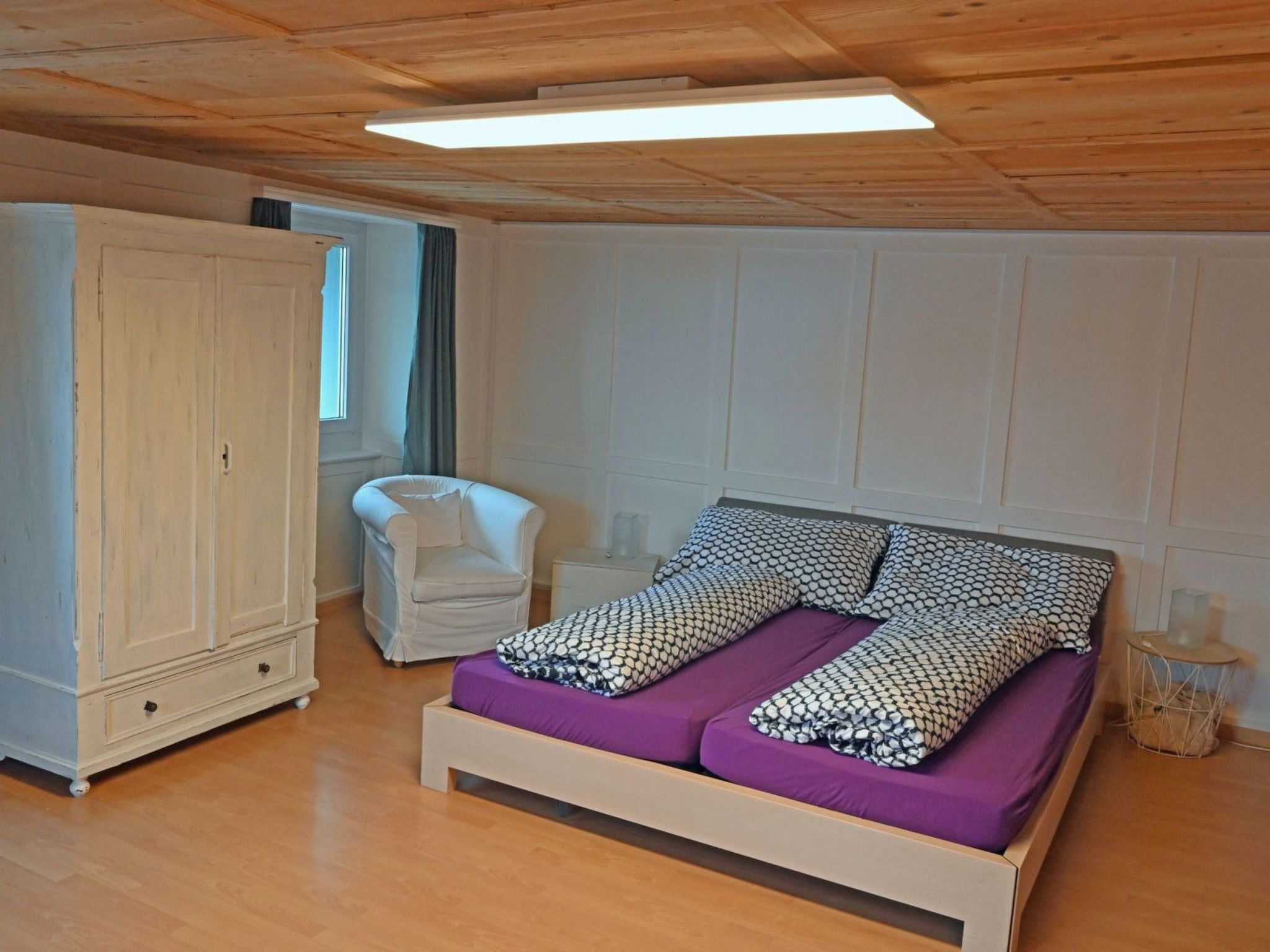 Un dormitorio con cama, armario, silla y mesita de noche.