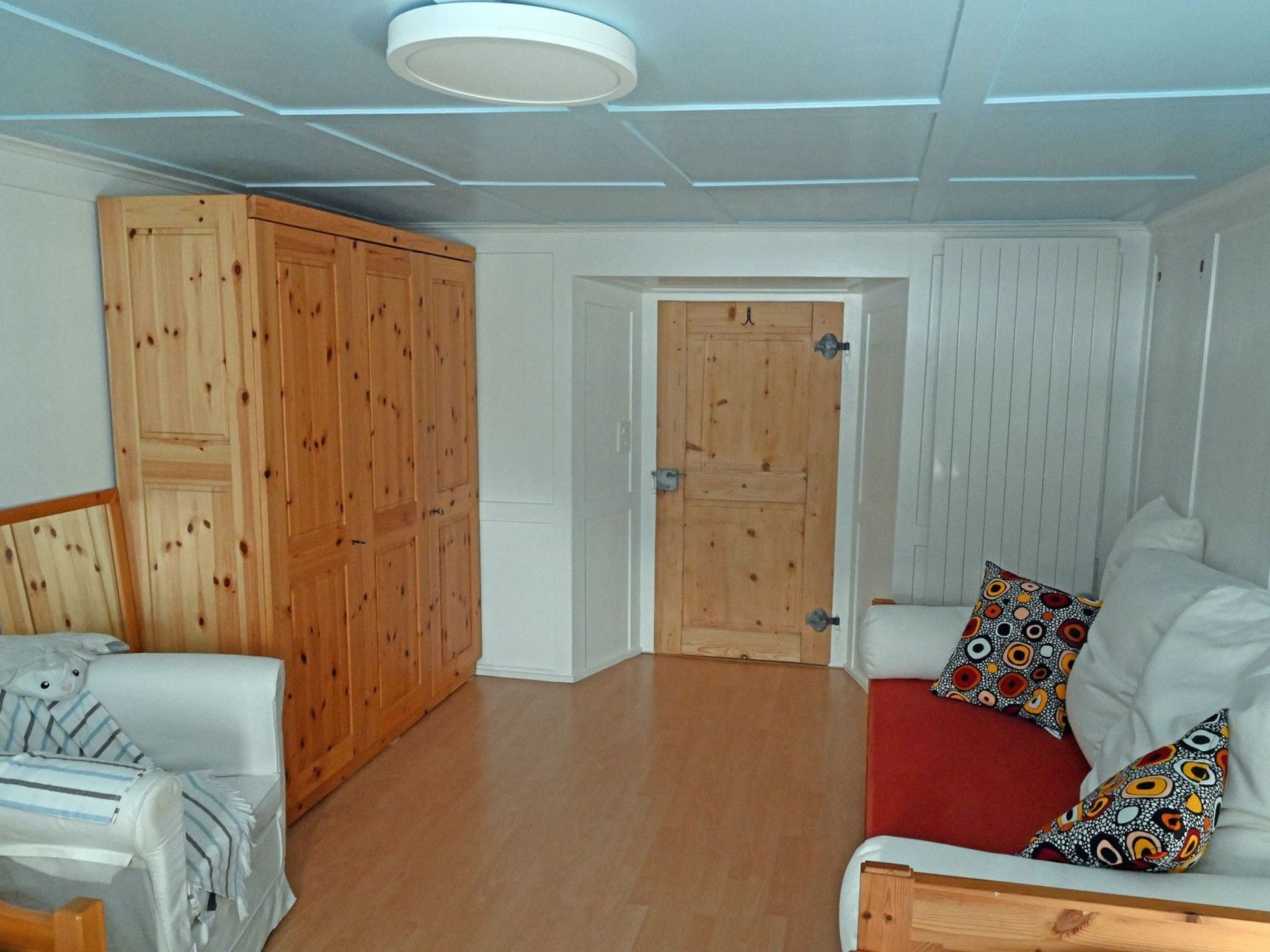 Una habitación con un armario de madera, un sofá blanco con cojines estampados y una manta roja.