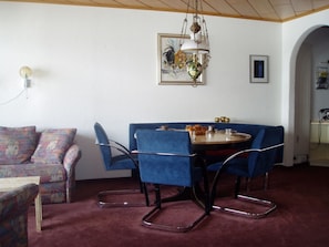 A dining area with a round table, blue upholstered chairs, a hanging light fixture, and a framed artwork on the wall. - Nodahüs Steiger, Obersaxen-Affeier, (Obersaxen), 34004B by Interhome (Obersaxen Affeier)