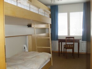 A bunk bed room with a desk and chair, a window with curtains, and a radiator. - Nodahüs Steiger, Obersaxen-Affeier, (Obersaxen), 34004B by Interhome (Obersaxen Affeier)