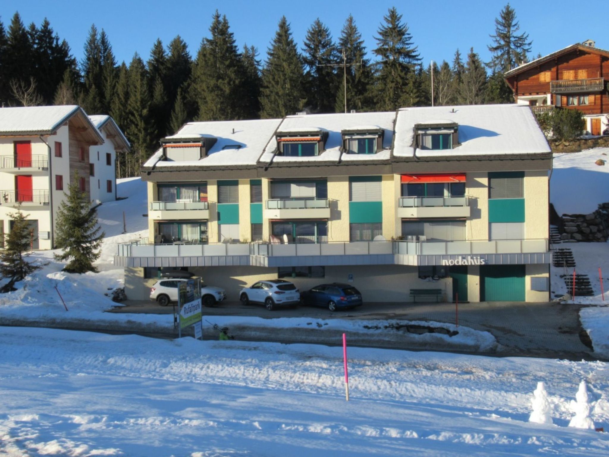 En byggnad med flera våningar, balkonger, en parkeringsplats och en snötäckt omgivning.