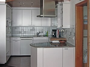 A compact kitchen with white cabinetry, a stainless steel range hood, and a tiled backsplash. - Nodahüs Steiger, Obersaxen-Affeier, (Obersaxen), 34004B by Interhome (Obersaxen Affeier)