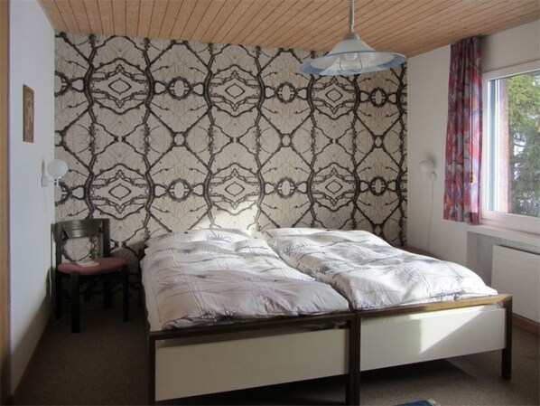 A single bed with a wooden frame in a room with a patterned wallpaper and a window with curtains.