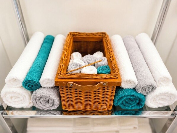 A storage area with neatly rolled towels in various colors and a wicker basket containing additional towels.