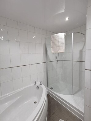 Un bany modern amb una banyera autònoma, dutxa amb envidriera i parets de rajola blanca.